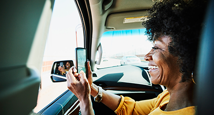 Woman of colour, taking a picture on mobile phone in passenger seat